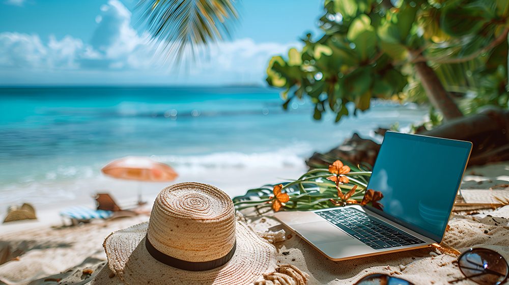 Laptop on a beach with turquoise water in the background — showing the freedom of working anywhere when you start a travel business